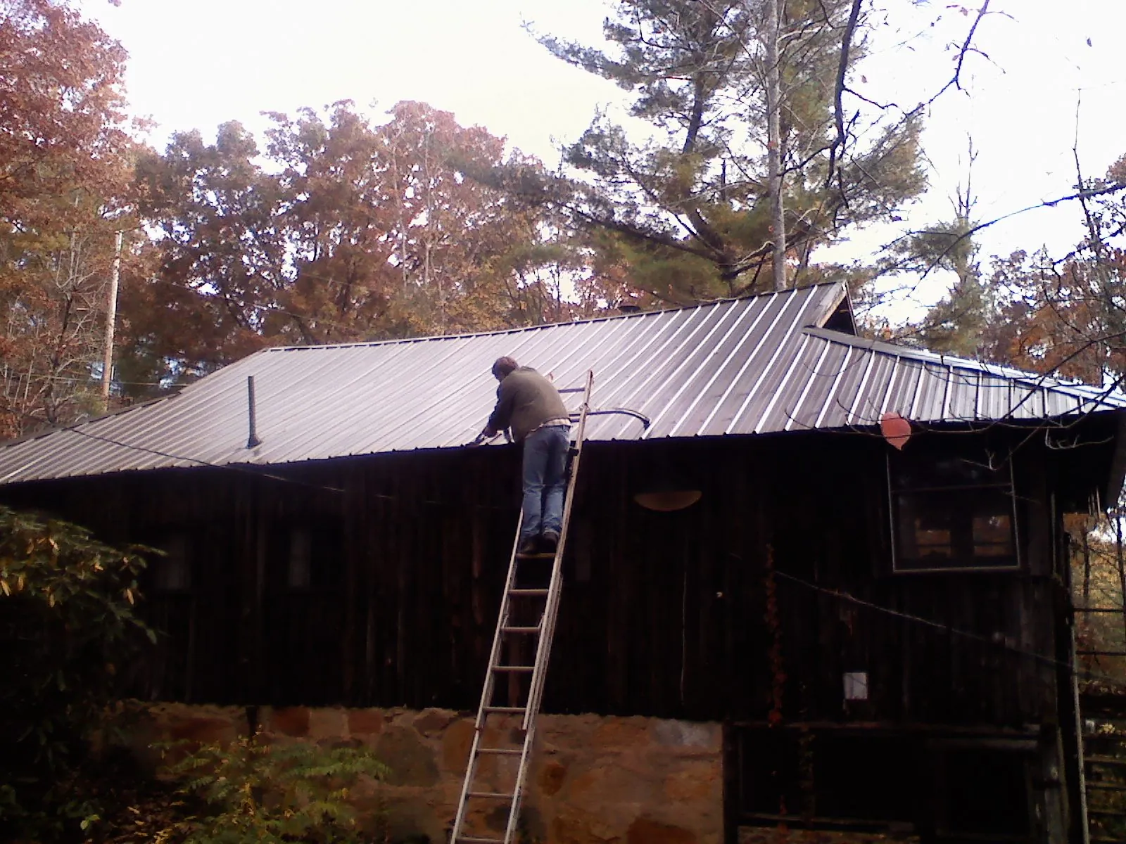 Roofer on a ladder working along the edge of a cabin metal roof in Augusta