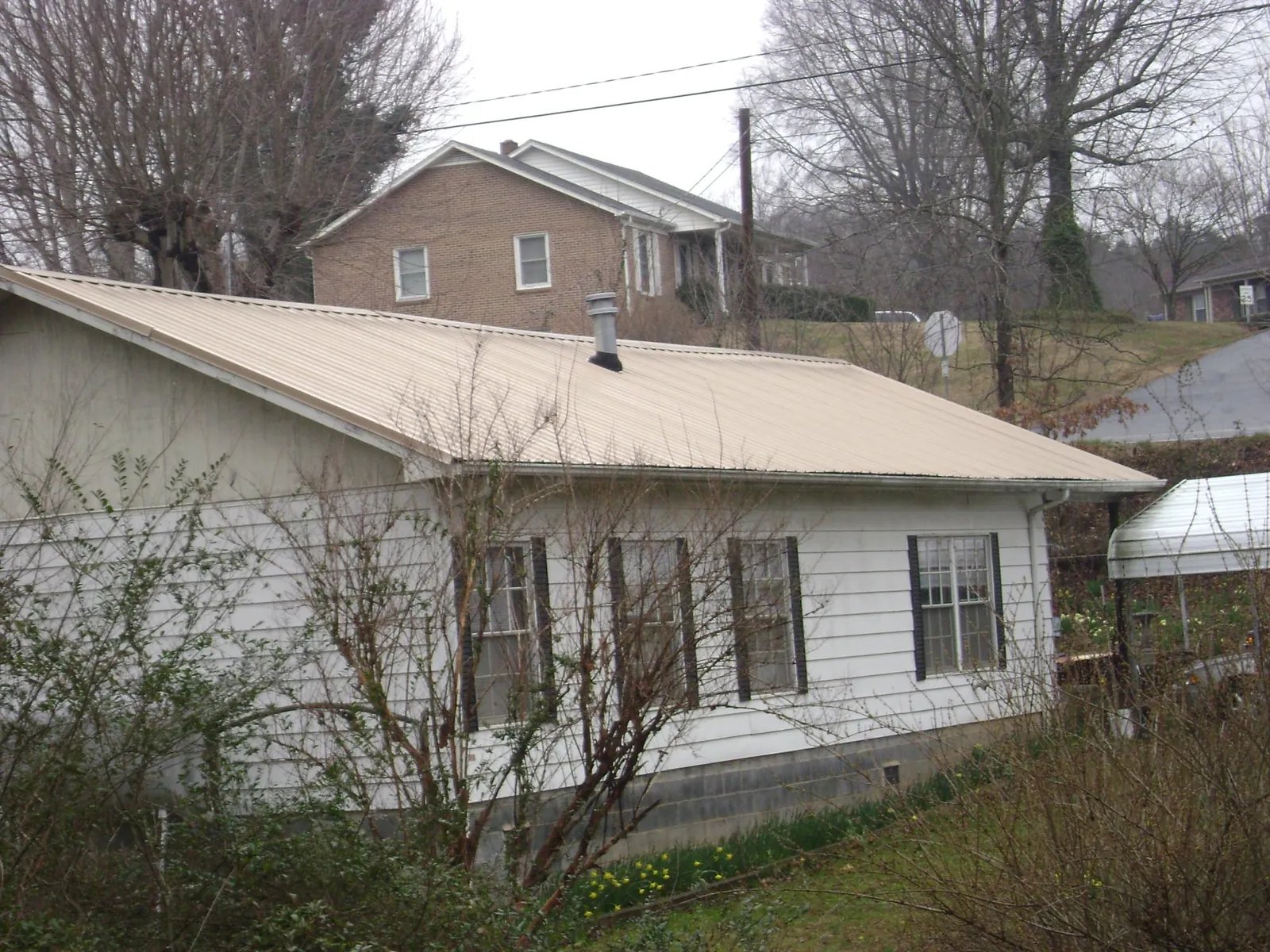 Tan metal roof on a white sided house set into a hillside — Commercial Roofing by Roofing Brothers in Augusta